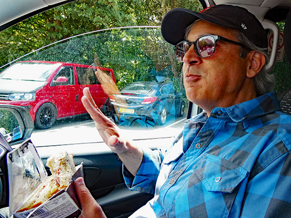 mike baggetta chowing a sandwich from and in a motorway service area